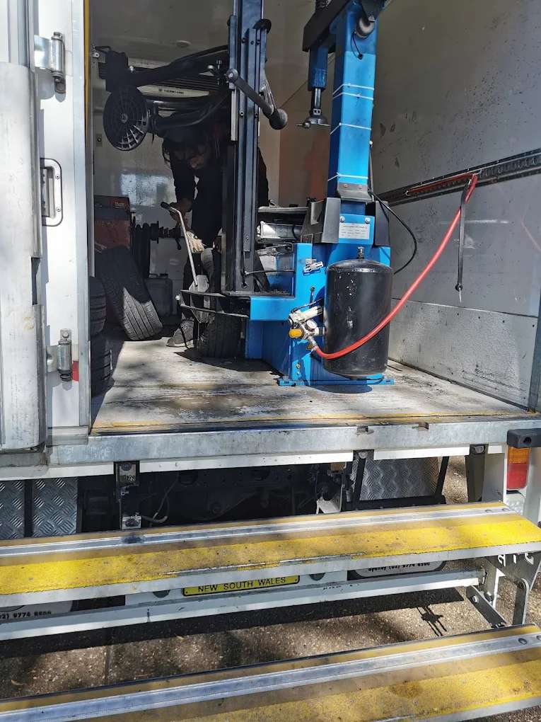 A technician at the tyre machine inside a Mobile Tyre World truck, with tyres stacked beside it